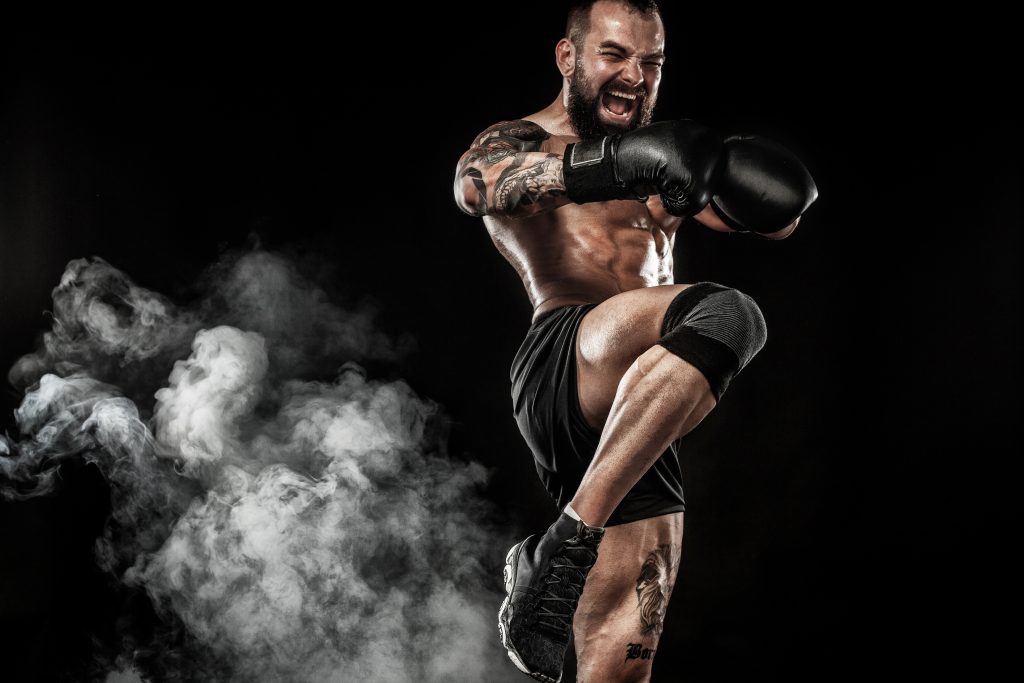 A man in boxing gloves doing a kick on a black background.