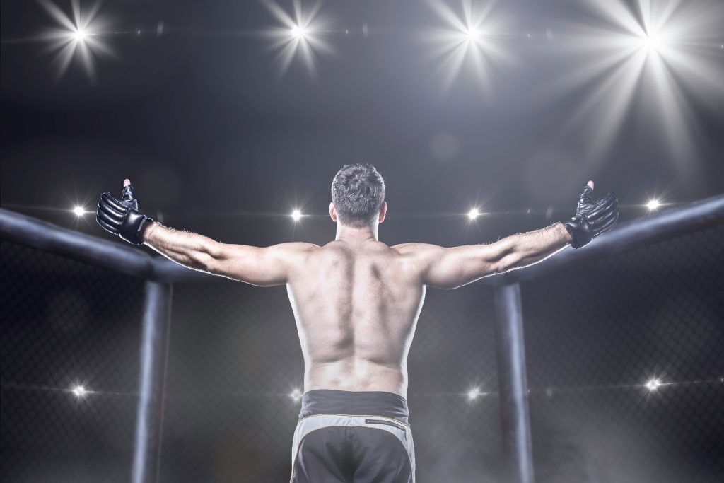 A man is standing in front of a cage with his arms raised.