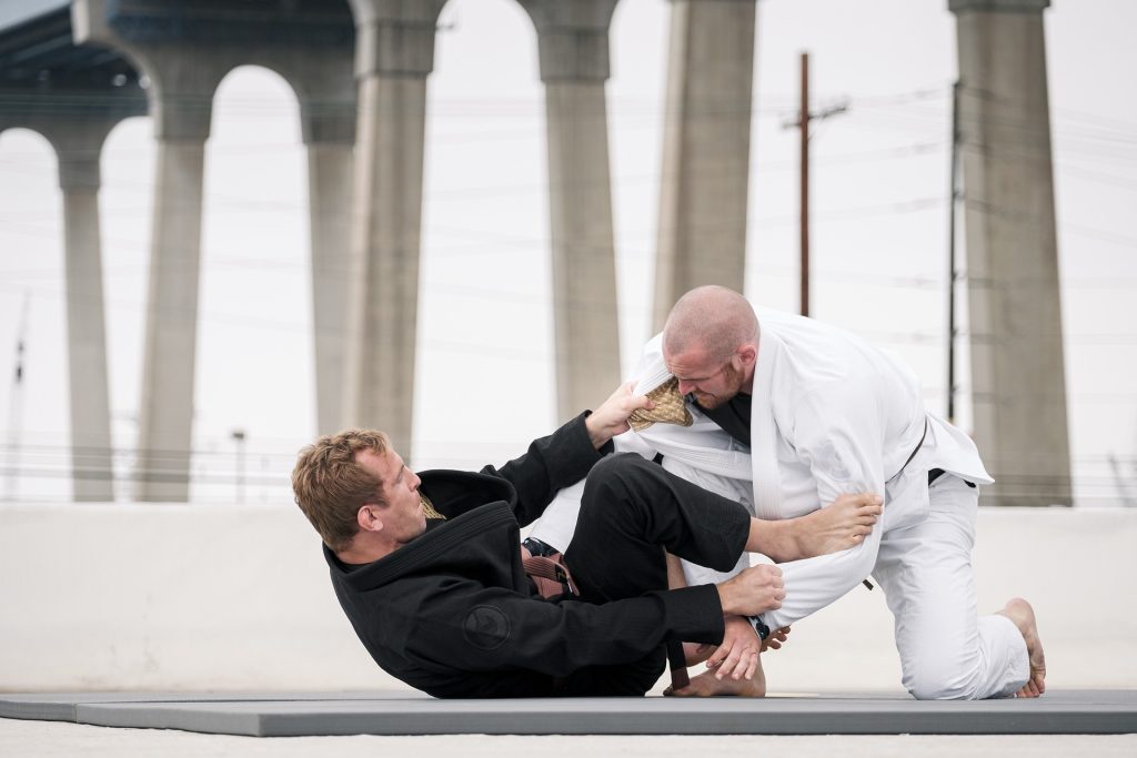 Two men doing jiu jitsu in front of a bridge.