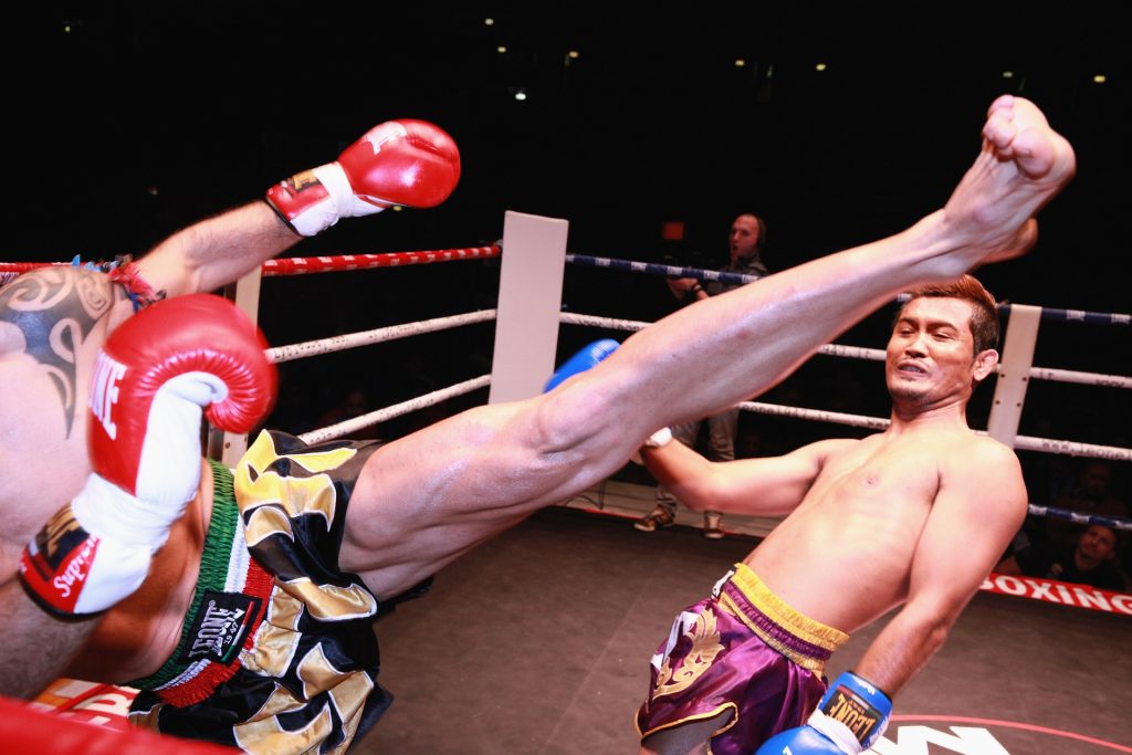 A man kicking another man in a boxing ring