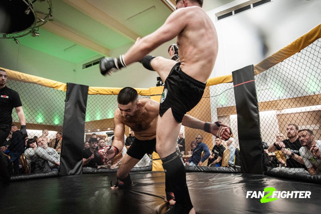 Two mixed martial arts fighters in a cage at an event, one dodging a high kick from the other.