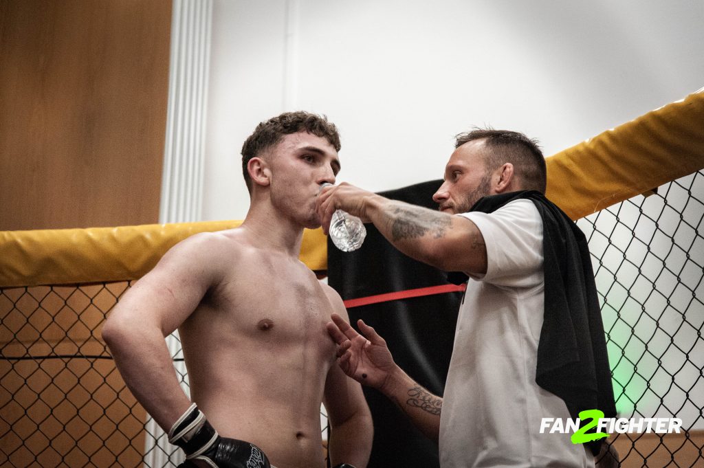 A male boxer receives water from his coach in a corner of a boxing ring during a break in training.