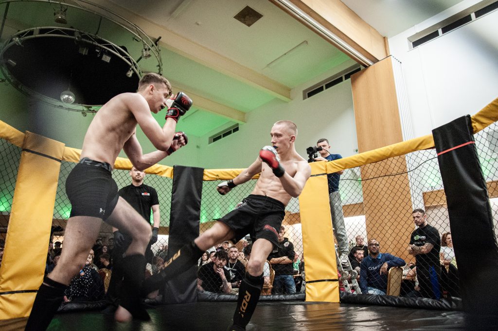 Two male mma fighters engage in a match inside a cage, with one throwing a punch at the other, as spectators watch closely around them.