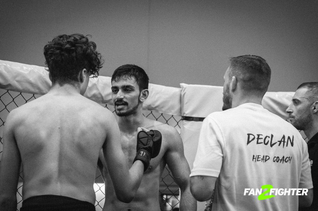 Three men in a mixed martial arts training session, with one raising his gloved hand and another with a beard.