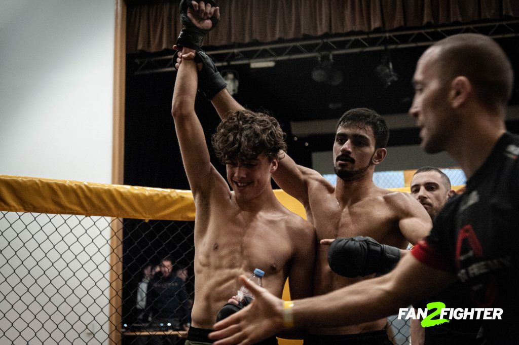 Two shirtless male fighters celebrate in an MMA cage, showcasing victory, camaraderie, and muscular builds.