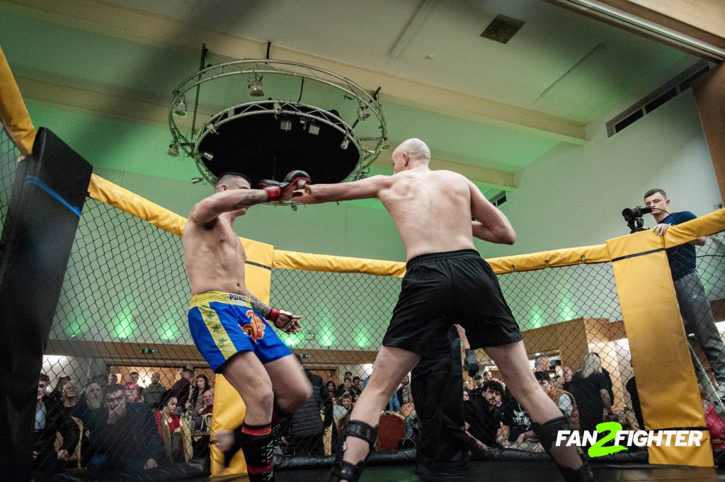 MMA fighters compete in a cage; one punches the other, with spectators and green lighting in the background.